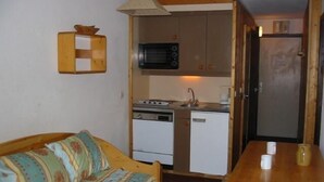 A compact kitchen with a microwave, stove, and refrigerator. There's a wooden table and a sofa with patterned cushions. - 200m from resort center, 4th floor, balcony, 28m², Val Thorens (Val Thorens)