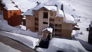 Un edificio de madera de varios pisos con balcones, rodeado de terreno nevado y montañas al fondo.