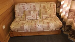 Ein Zimmer in einer Holzhütte mit einem Bett, das mit gemusterten Bettwaren bezogen ist.
