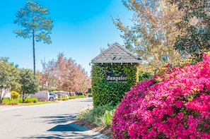 Un bungalow agrémenté d’une enseigne, entouré de fleurs roses éclatantes et surplombé par un ciel d’un bleu limpide.