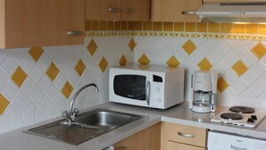 Uma cozinha compacta com armários de madeira, micro-ondas, cafeteira e lava-louças.