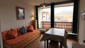 Um quarto aconchegante com um sofá de madeira, uma mesa e vista para uma paisagem montanhosa através de grandes janelas.