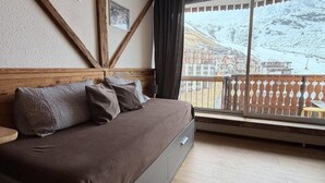 Een slaapkamer met een houten hoofdbord, een groot raam met uitzicht op een besneeuwde berg en een balkon met een hekwerk.