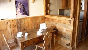 Een houten eetruimte met een tafel voor vier personen, stoelen en een schilderij aan de muur.