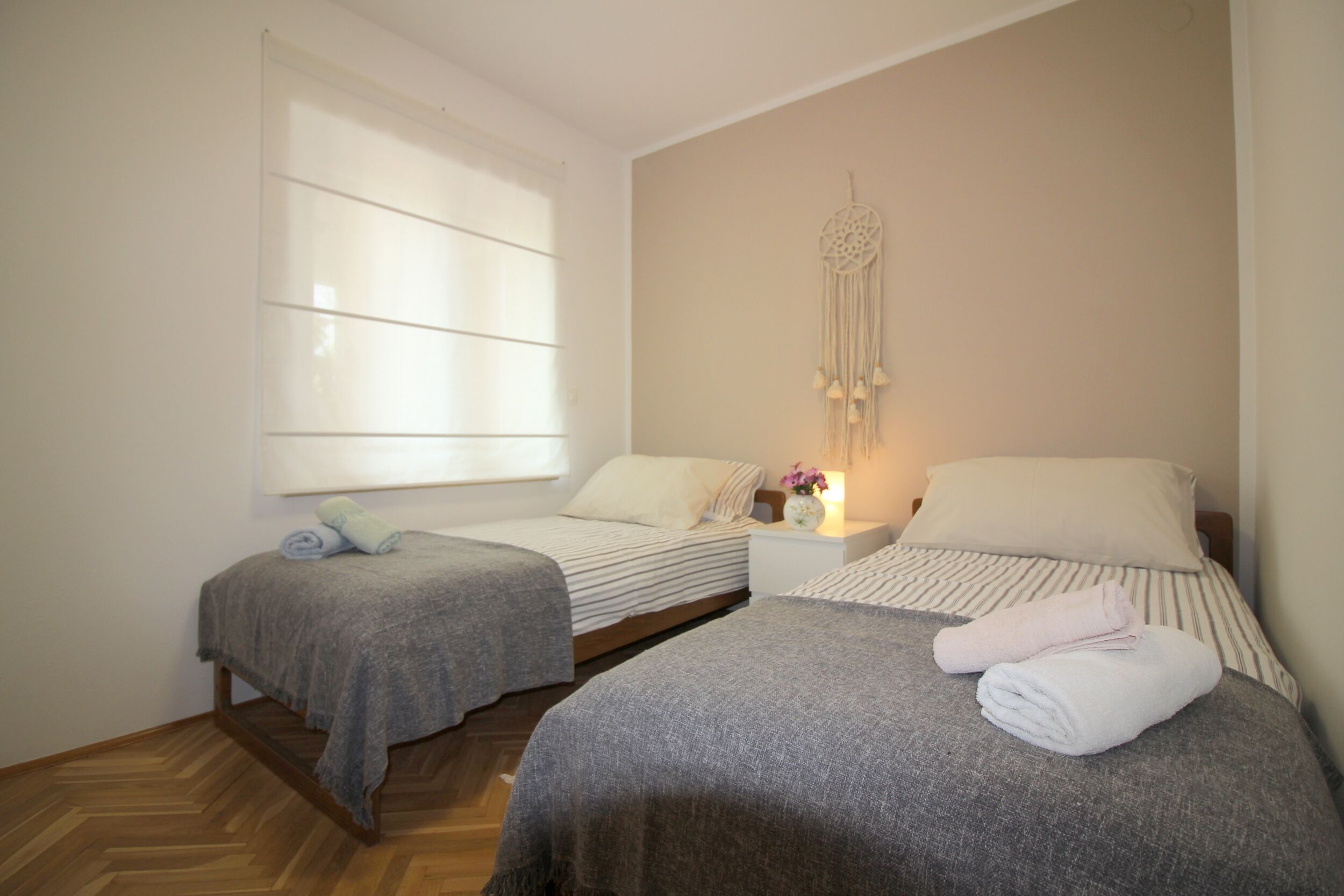 Une chambre avec deux lits simples, une grande fenêtre et un attrape-rêves fixé au mur.