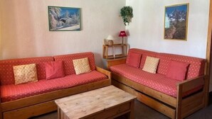 A cozy living room with two red sofas, a wooden coffee table, and two framed pictures on the walls.