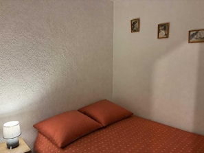 A single bed with two pillows, a small bedside table with a lamp, and three framed pictures on the wall.
