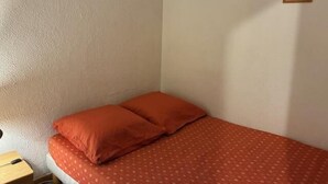 A small, single-bed room with a red bedspread and matching pillows. There are three framed pictures on the wall.