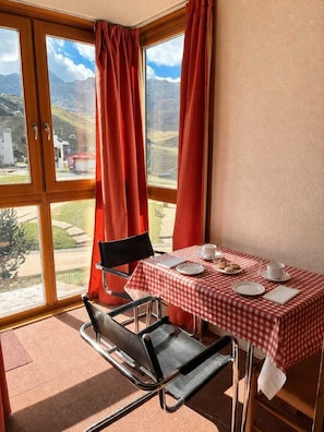 A room with a table set for two, a chair, and a view of the outdoors.