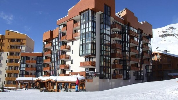 A multi-story hotel with balconies and large windows, situated in a snowy area with a mountain in the background.