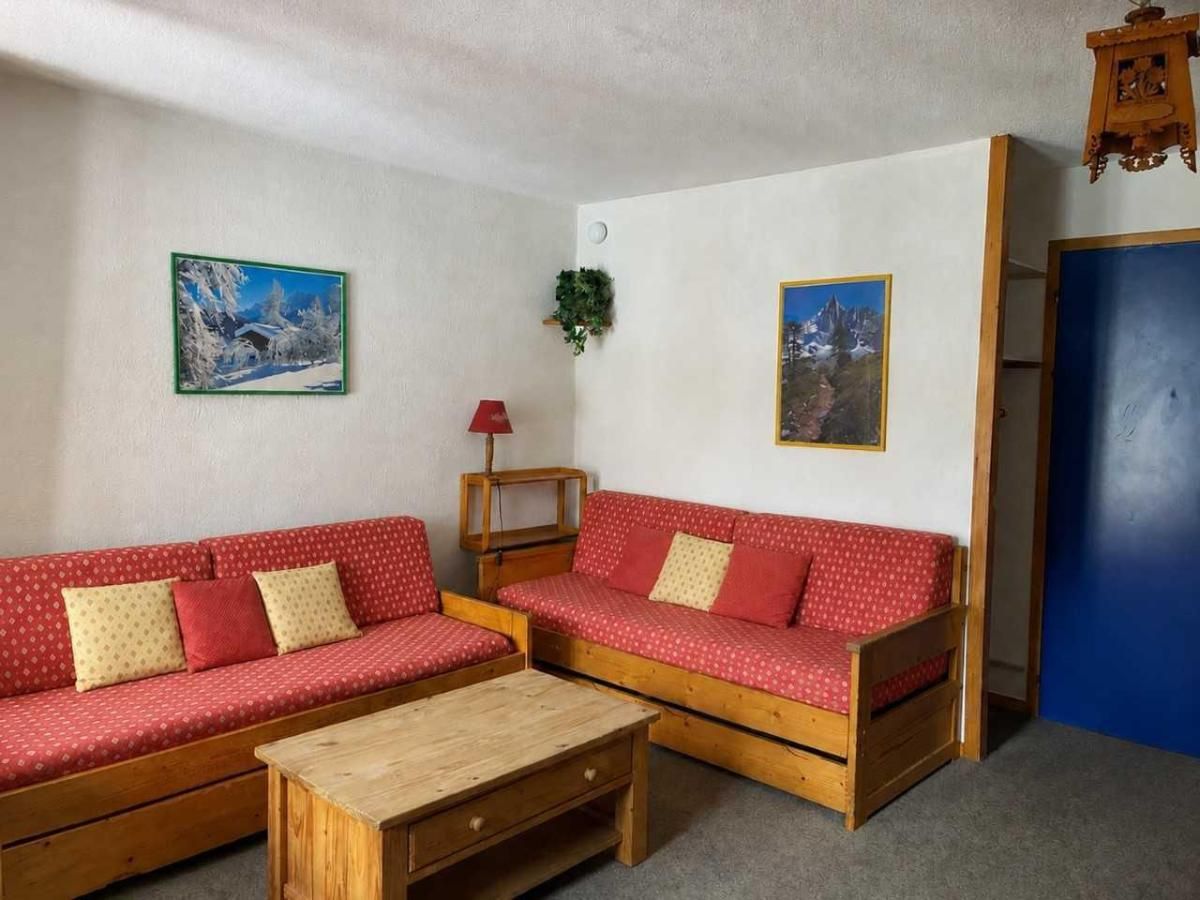 A room with two red sofas with patterned cushions, a wooden coffee table, and two wall-mounted paintings.