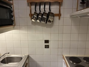 A kitchen with white tiles, a built-in oven, a sink, and hanging pots.