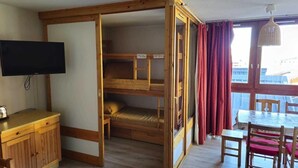 A compact room with a bunk bed, a TV, a wooden desk, and a dining table with chairs. - 10m from resort center, 2nd floor, tv, 30m², Val Thorens (Val Thorens)