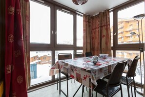A dining area with a table set for two, large windows, and a view of buildings outside.