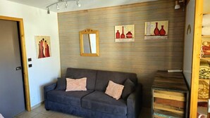 Ein Wohnzimmer mit grauem Sofa, Holzvertäfelung und drei gerahmten Kunstwerken.