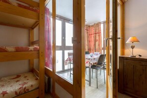 A room with bunk beds, a dining area with a table and chairs, and a lamp on a cabinet.