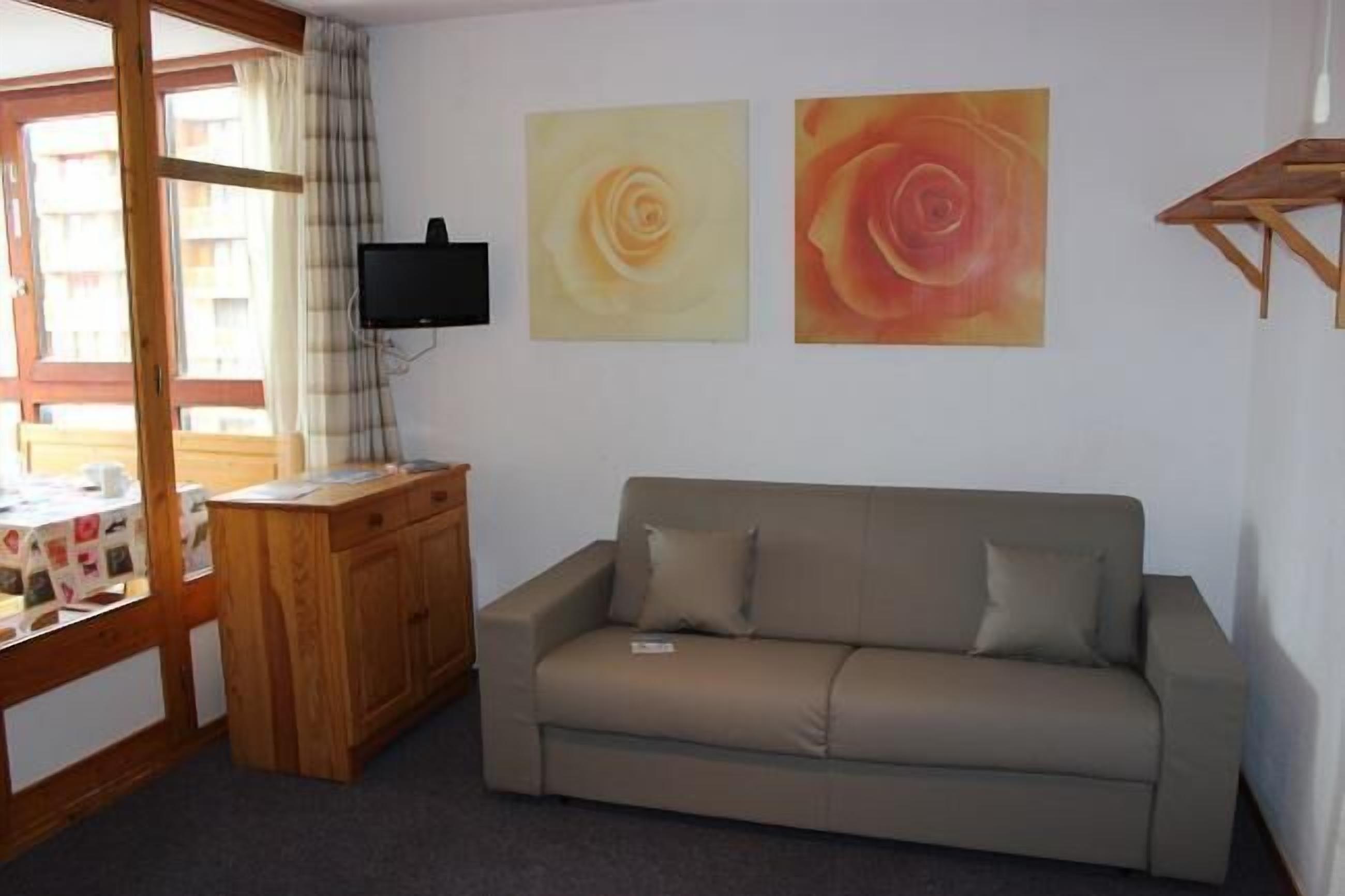 A room with a beige sofa, wooden desk, and two paintings of roses.
