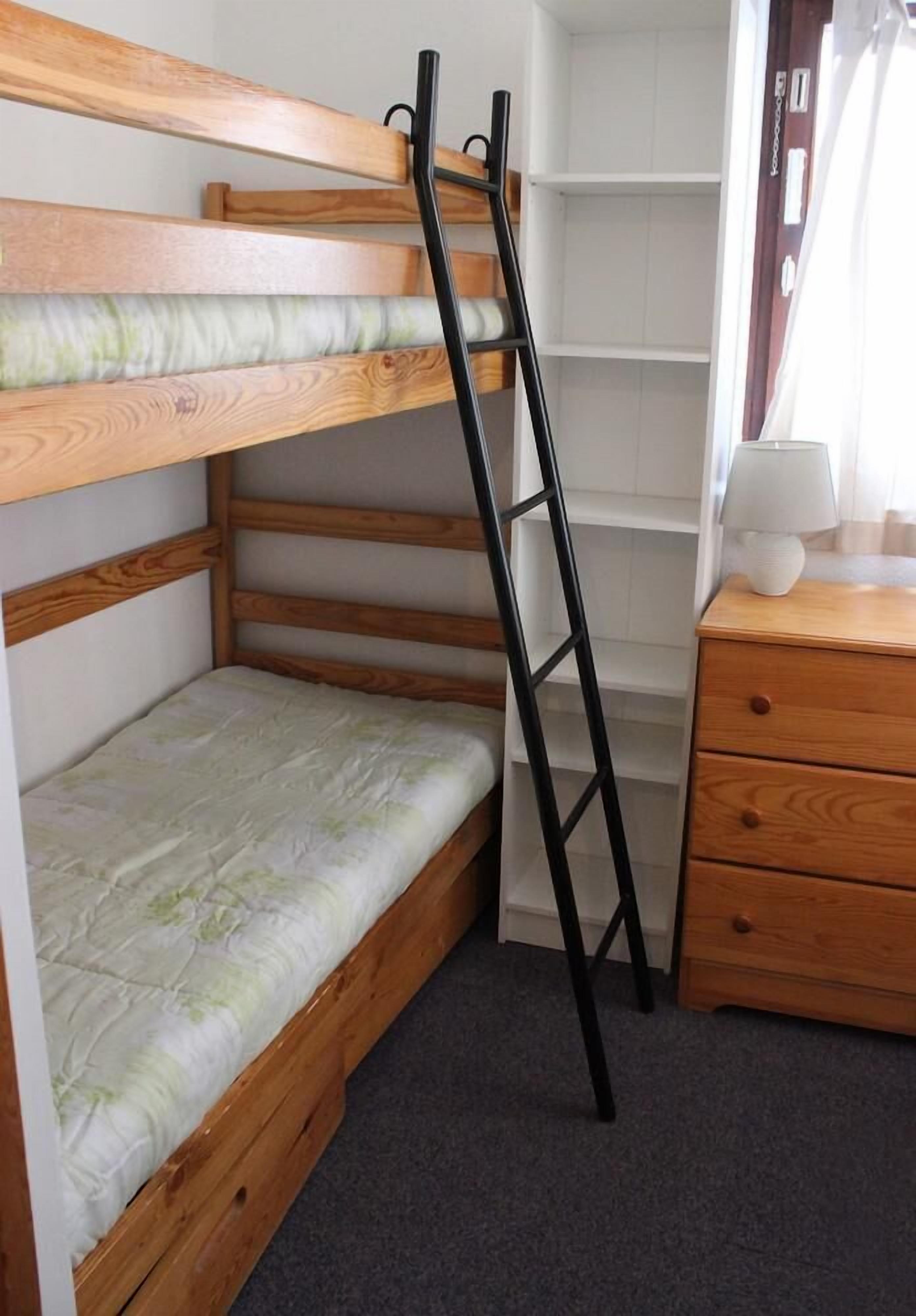 Una cama litera con escalera, un aparador de madera y una lámpara.