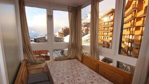 Une chambre avec un lit, une fenêtre avec des rideaux et une vue sur des bâtiments enneigés.