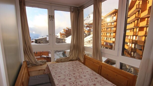 A room with a bed, a window with curtains, and a view of snow-covered buildings. - 50m from ski slopes, 4th floor, balcony, tv, 30m², Val Thorens (Val Thorens)