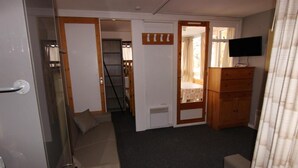 Une pièce de taille modeste, comprenant un canapé, une commode en bois, un téléviseur et une porte donnant sur une autre pièce.