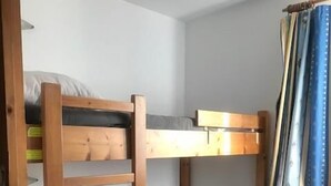 A bunk bed room with a wooden frame, grey mattress, and a small wooden shelf. - 50m from ski slopes, 5th floor, tv, 35m², Val Thorens (Val Thorens)