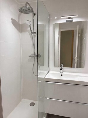 Ein modernes Badezimmer mit einer gläsernen Dusche, einem weißen Waschbecken und einem Spiegel darüber.