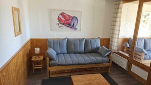 Un'accogliente stanza con un divano con struttura in legno, un tavolino con una lampada e un quadro appeso al muro.