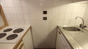 Una cucina compatta con pareti piastrellate di bianco, un lavello in acciaio inossidabile e un piano cottura integrato.