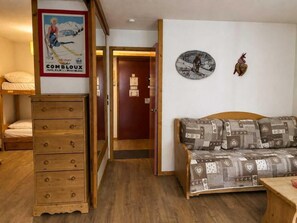 Una stanza con un comò in legno, un divano con motivi decorativi, una sveglia a parete e una porta che dà su un'altra stanza.