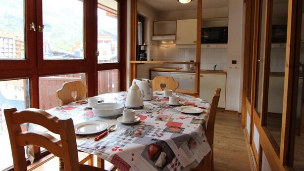 A dining area with a table set for four, wooden chairs, and a view through a glass door to the kitchen. - 50m from ski slopes, 6th floor, balcony, tv, 35m², Val Thorens (Val Thorens)