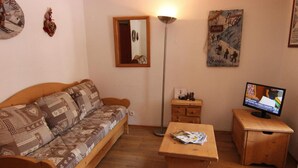 A cozy living room with a wooden sofa, a small wooden table, a TV, and a floor lamp. - 50m from ski slopes, 6th floor, balcony, tv, 35m², Val Thorens (Val Thorens)