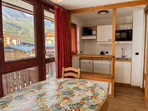 A room with a dining table, a chair, a kitchen area with a microwave, and a view of mountains through a window.