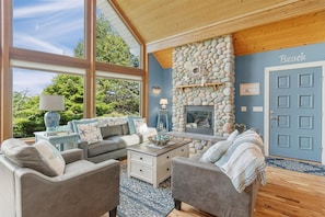 A cozy living room with a stone fireplace, large windows, and a blue door labeled "Beach". - Pets OK, 150 yds to beach, modern, luxury (Journey) (Ocean Park)