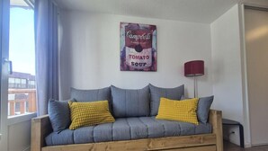 A grey sofa with wooden legs, two yellow pillows, and a red lamp on a white wall. - 100m from ski slopes, balcony, tv, 23m², Val Thorens (Val Thorens)