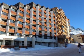 A multi-story hotel with balconies, a ski resort in the background, and a person skiing.