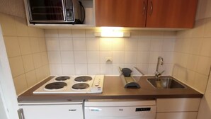 Une cuisine compacte équipée d’une cuisinière, d’un évier et d’un lave-vaisselle, avec des meubles blancs et un dosseret carrelé.