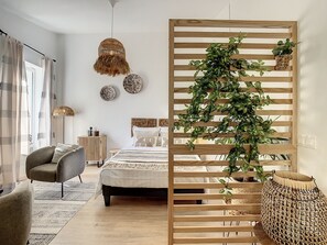 A modern bedroom with a bed, a chair, a bedside table, a hanging light, and a wooden partition with plants.