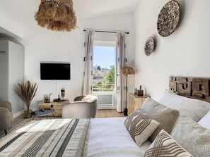 Een slaapkamer met een groot bed, een televisie, een raam met gordijnen en uitzicht op buiten.