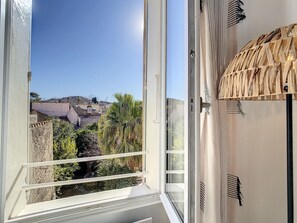 Een kamer met een groot raam met uitzicht op een stadsbeeld, een geweven plafond en een witte muur.