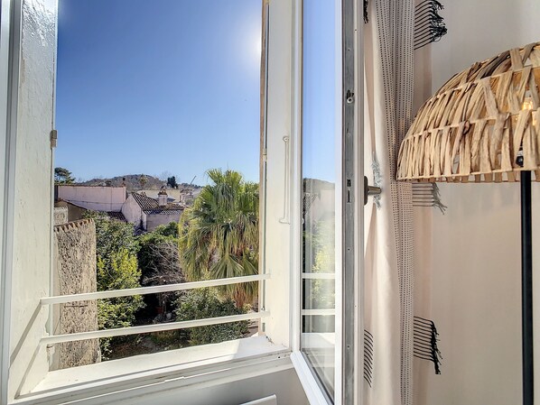 A room with a large window overlooking a cityscape, a woven ceiling, and a white wall.