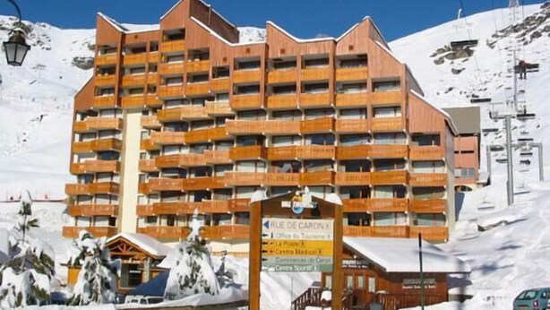 Hotel de varios pisos con balcones, un telesilla de esquí al fondo y un cartel que indica servicios como centro médico y spa.