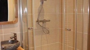 Ducha en esquina con cabina de vidrio, tocador de madera con lavabo tipo cuenco y espejo sobre el lavabo.