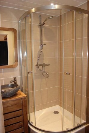 A corner shower with a glass enclosure, a wooden vanity with a bowl sink, and a mirror above the sink.