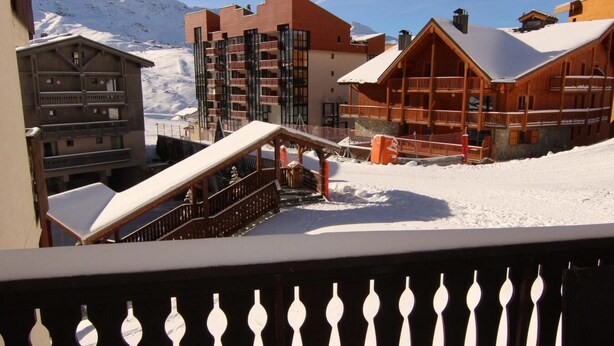 Een besneeuwde buitenplaats met houten gebouwen, waaronder een lodge met balkon en een gebouw met meerdere balkons.