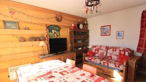 Een gezellige kamer met een houten wand, een televisie, een bank met een rood-wit gestreept deksel, en een houten kast met diverse spullen.