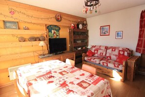 A cozy room with a wooden wall, a television, a sofa with a red and white patterned cover, and a wooden cabinet with various items.