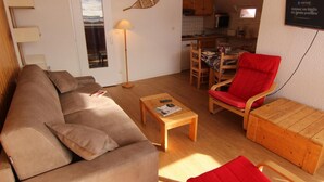 Een woonkamer met een bank, een rode fauteuil, een houten salontafel en een lamp.