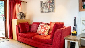 A red sofa with multiple cushions, a wooden side table, a basket on a wooden cabinet, and a painting on the wall. - Characterful Semi-Detached House; Enviably Located (St Andrews)