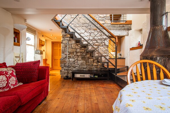 A cozy living room with a red sofa, a wooden dining table, and a stone staircase leading to an upper level.